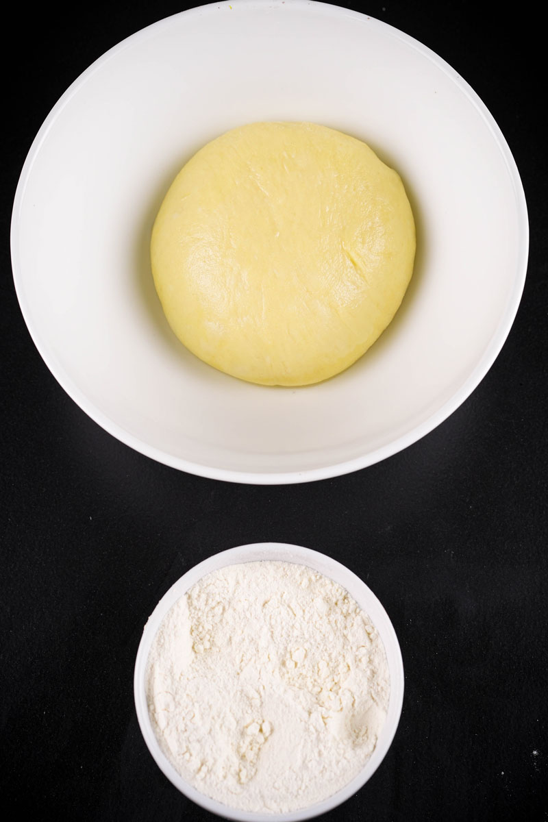 Soft naan dough resting in a white bowl with flour on the side