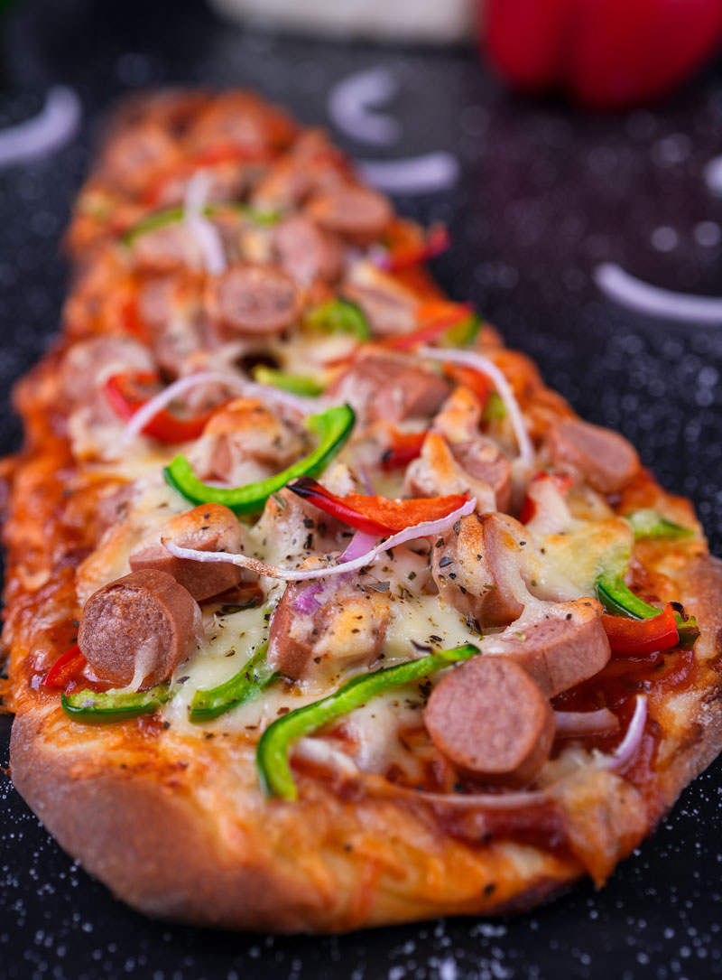 Close-up of cheesy naan pizza topped with sausages, bell peppers, and onions.