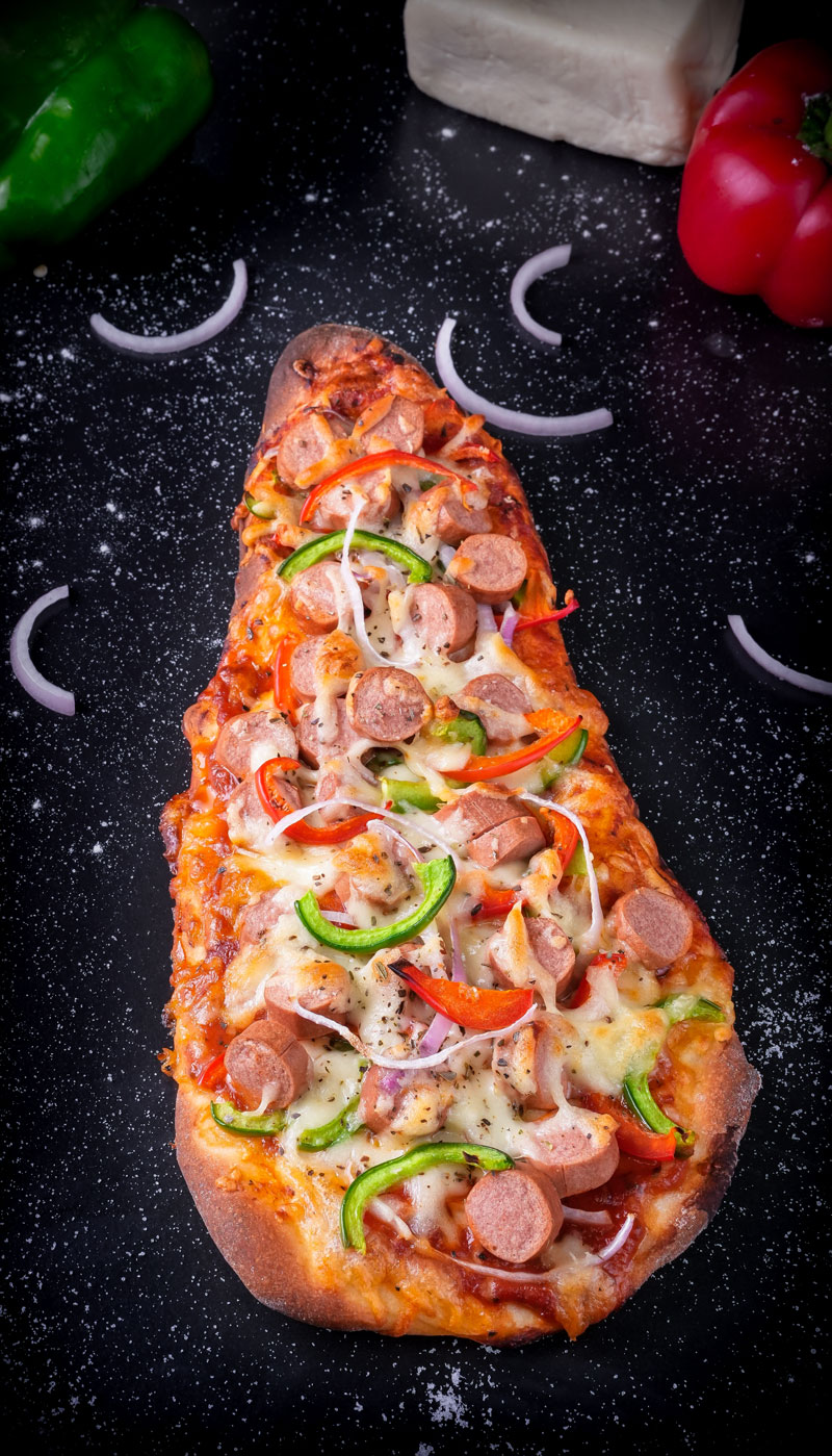 Whole naan pizza with melted cheese and colorful toppings on a black surface.