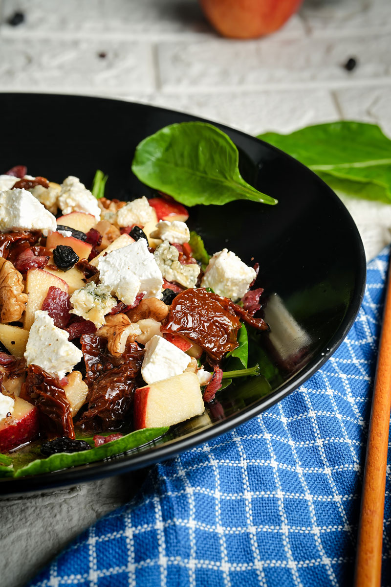 Close-up of apple pecan salad with feta cheese, spinach, and sun-dried tomatoes in a black bowl