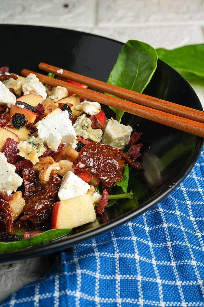 Close-up of apple pecan salad with feta cheese, spinach, and sun-dried tomatoes in a black bowl