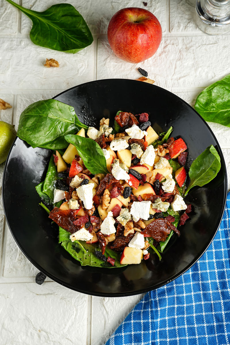 Top view of apple pecan salad with fresh apples, spinach, and feta cheese on a white textured background