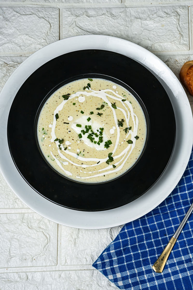 Overhead view of creamy leek potato soup garnished with herbs and cream, served in a black bowl.