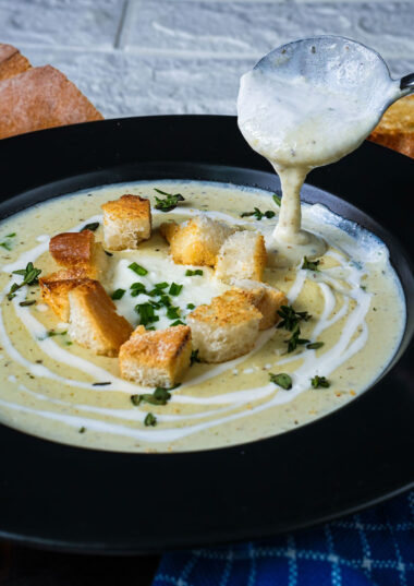 Creamy leek potato soup being served with croutons and fresh herbs.