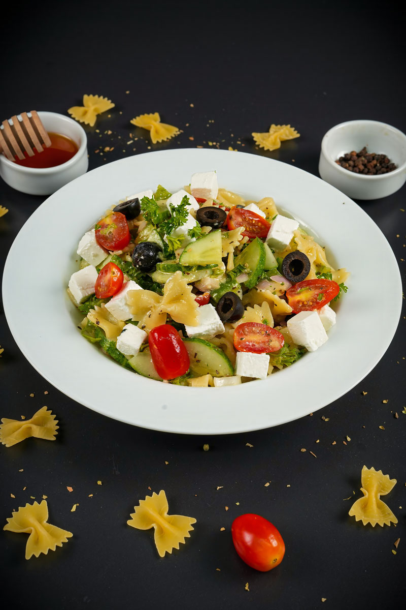 Homemade Greek pasta salad with fresh vegetables and raw farfalle pasta garnish