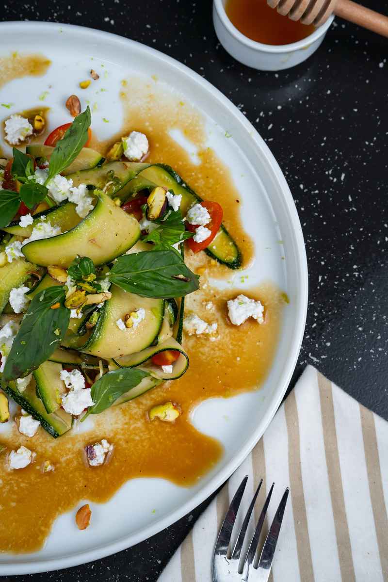 Overhead view of raw zucchini salad with honey dressing drizzled on a white plate.