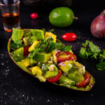 Avocado kiwi salad served in an avocado shell with lime and onion in the background.