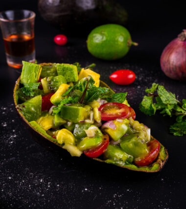 Avocado kiwi salad served in an avocado shell with lime and onion in the background.