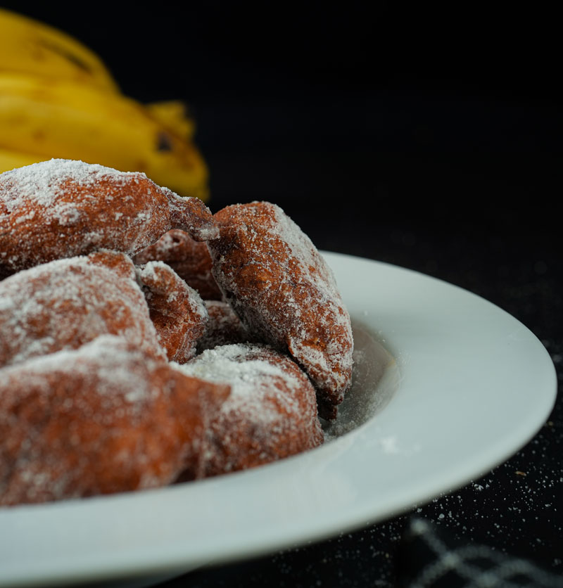 Banana fritters on a plate dusted with powdered sugar