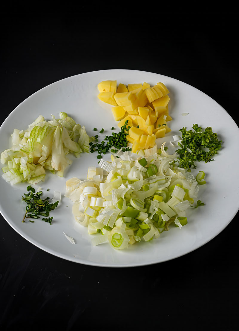 Chopped leeks, potatoes, and herbs prepared for creamy leek potato soup.