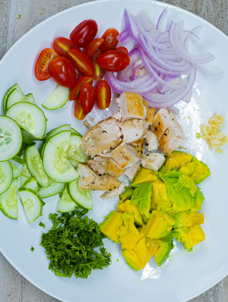 Fresh ingredients for grilled chicken avocado salad on a white plate.