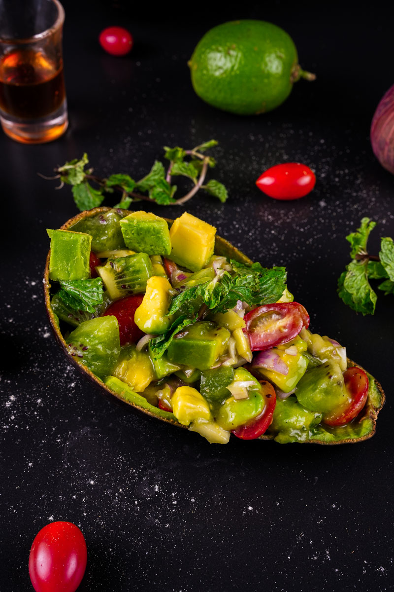 Fresh avocado kiwi salad with cherry tomatoes and mint in an avocado shell.