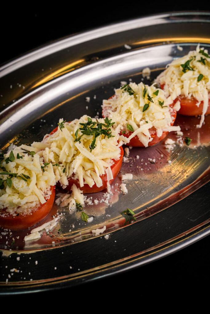 Sliced tomatoes topped with grated cheese and herbs on a silver tray.