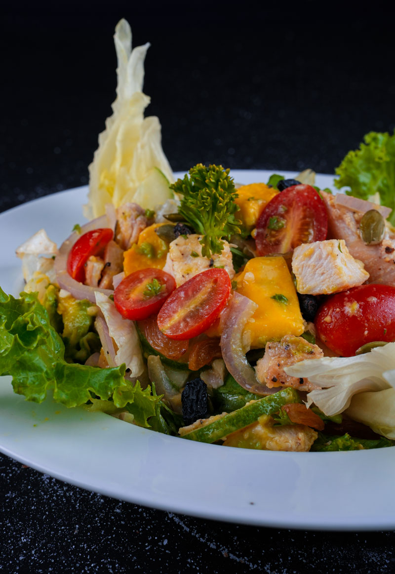 Grilled chicken avocado salad with cherry tomatoes and mixed greens on a white plate.