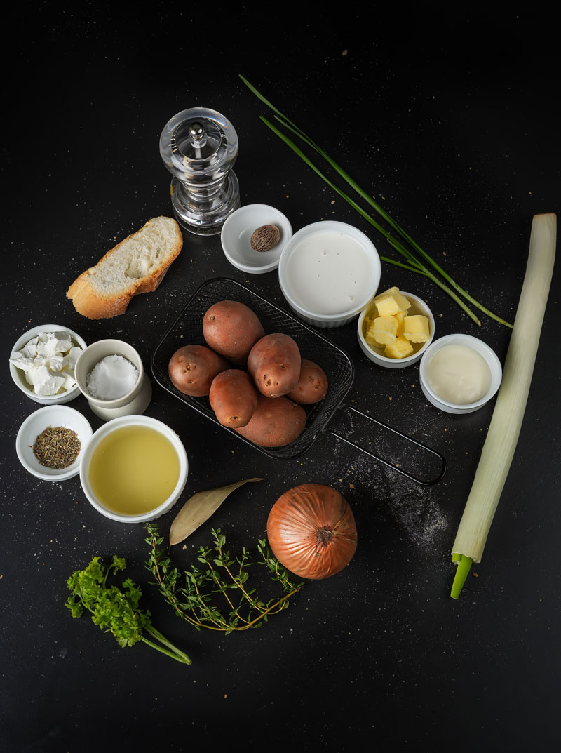 Ingredients for creamy leek potato soup arranged on a dark surface.