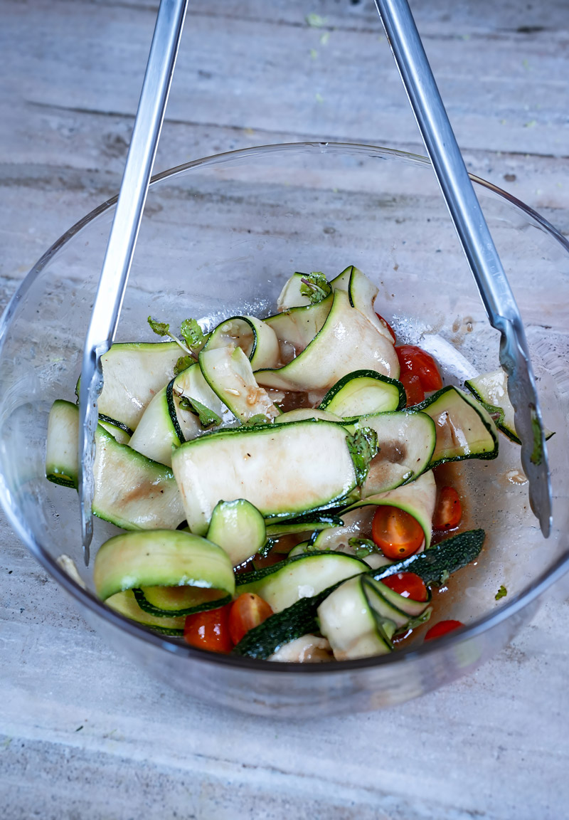 Fresh zucchini ribbons and cherry tomatoes tossed in a light vinaigrette in a glass bowl.