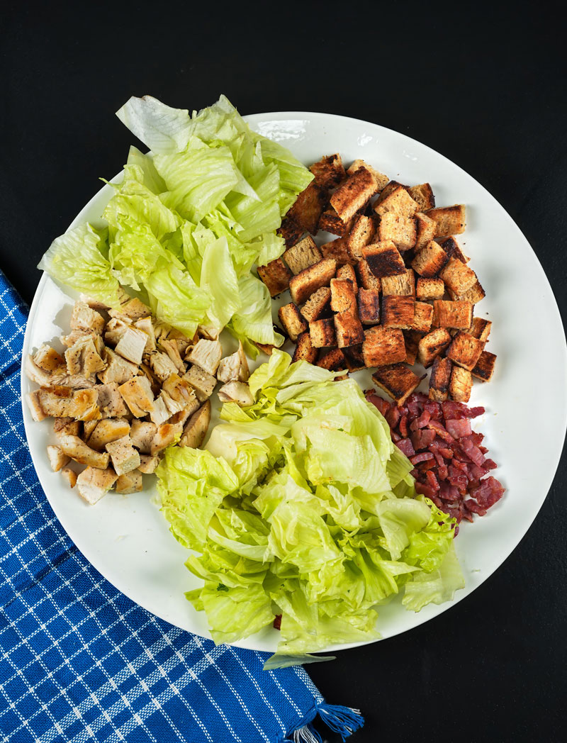 Deconstructed Chicken Caesar Salad components: grilled chicken, lettuce, croutons, and bacon.