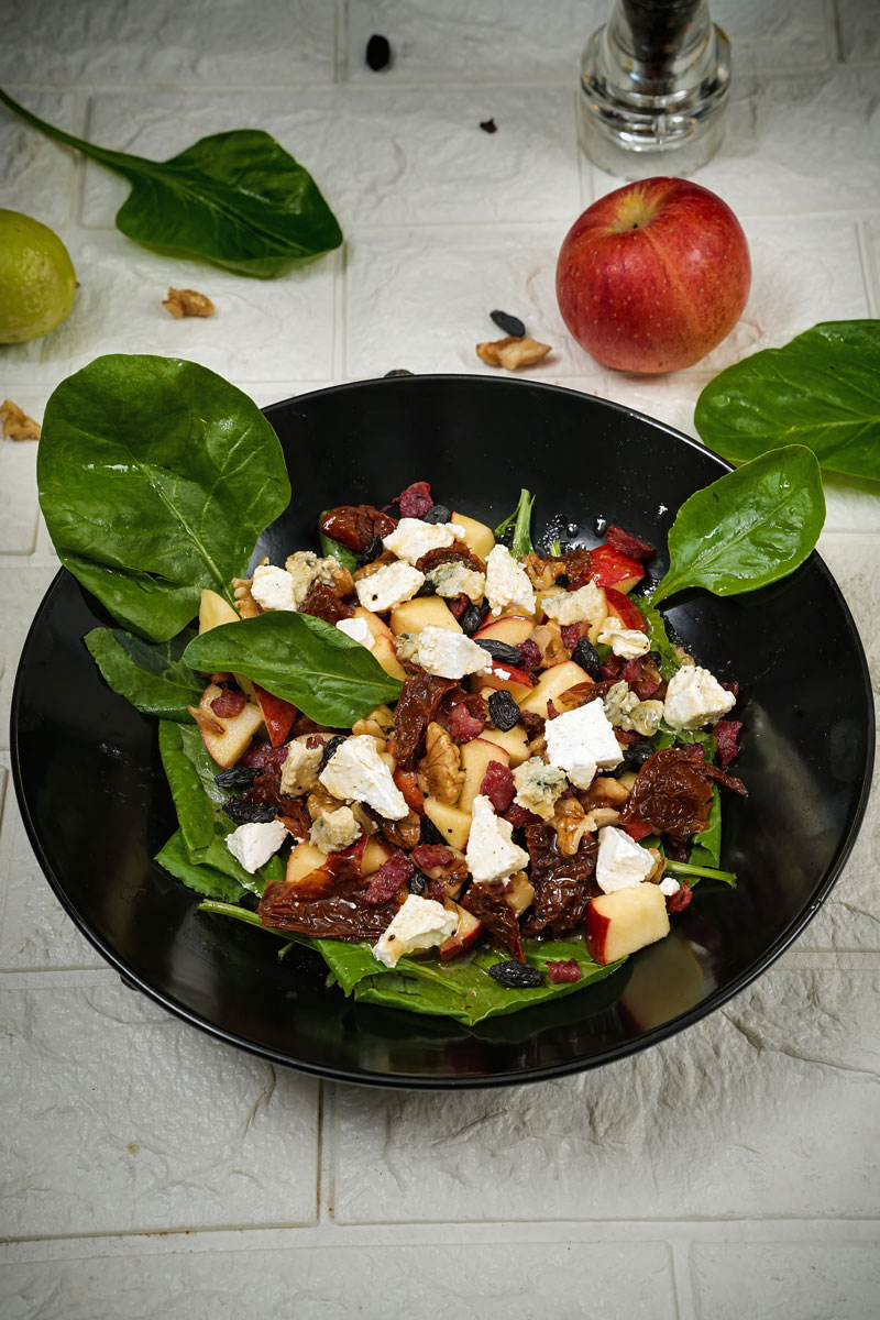 Apple pecan salad garnished with spinach leaves and fresh apple on a textured surface