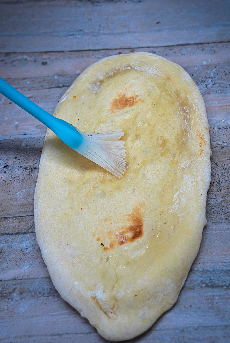 Naan base brushed with oil, ready for tandoori paneer pizza toppings