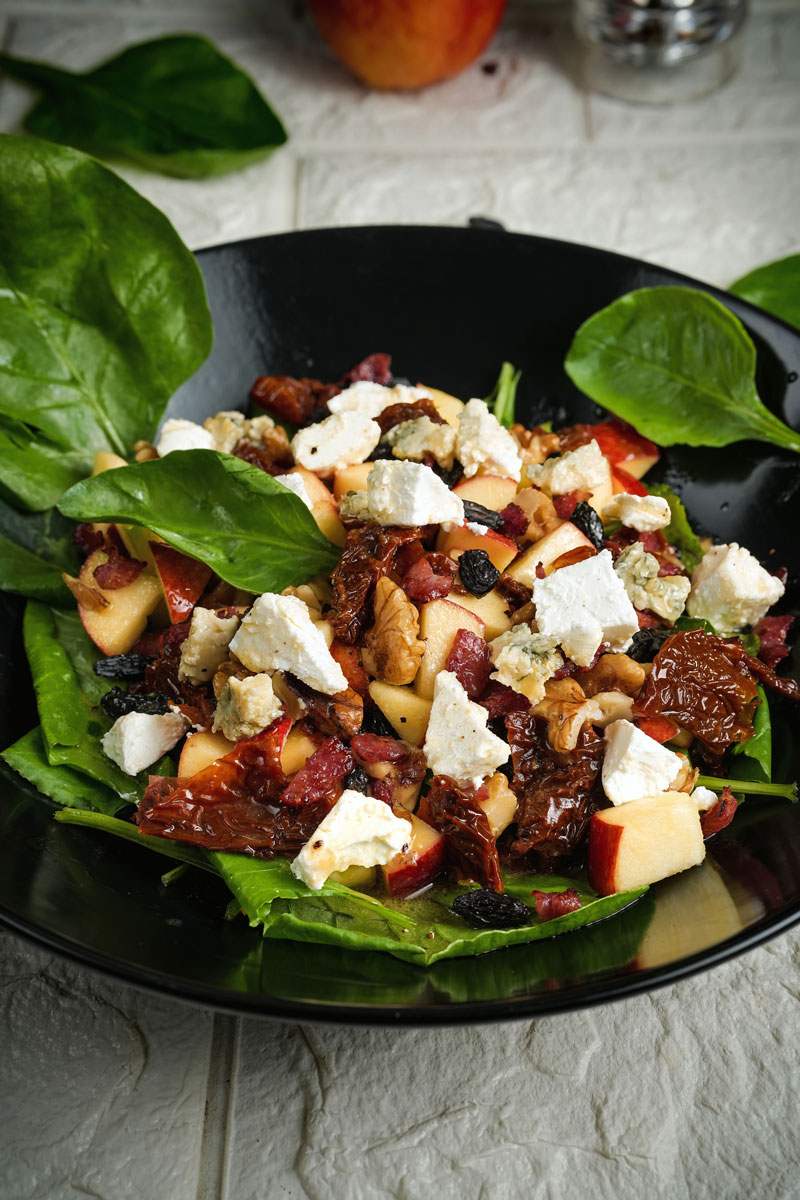 Close-up of apple pecan salad with spinach, walnuts, and feta cheese in a black bowl