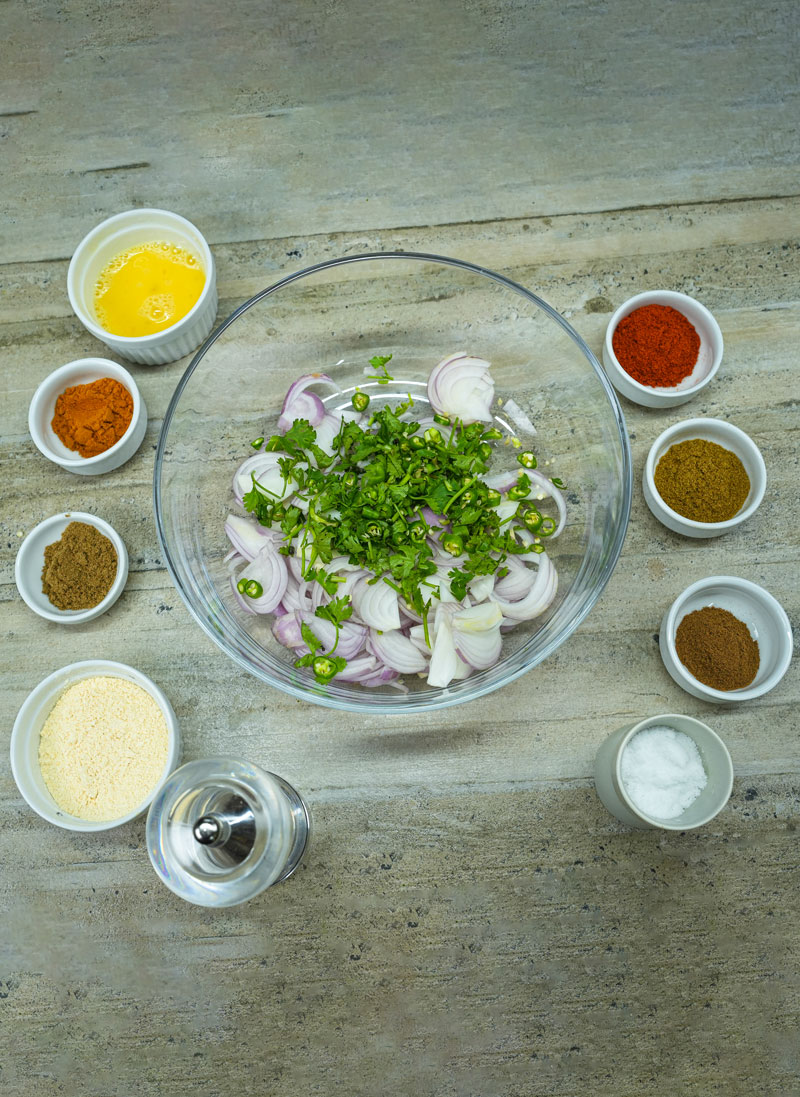 Ingredients for onion fritters in a bowl with spices around