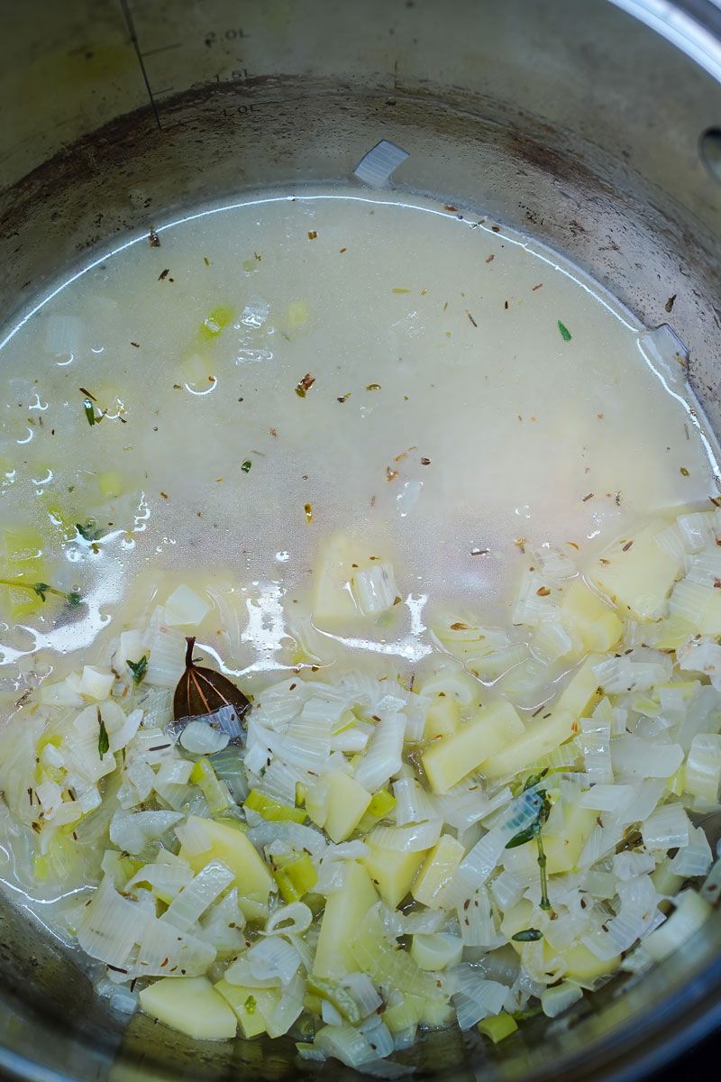 Pot of simmering leeks, potatoes, and herbs for creamy leek potato soup.