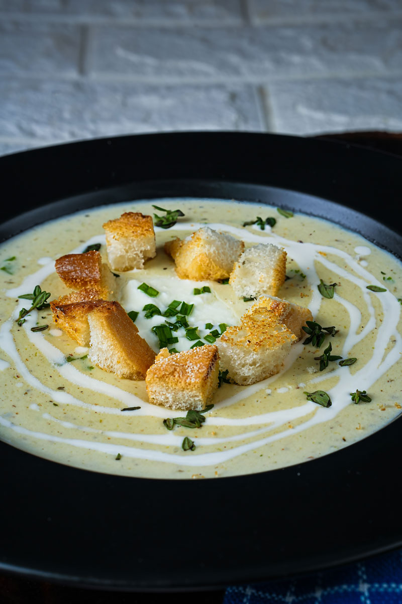 Bowl of creamy leek potato soup topped with croutons, fresh herbs, and a swirl of cream.