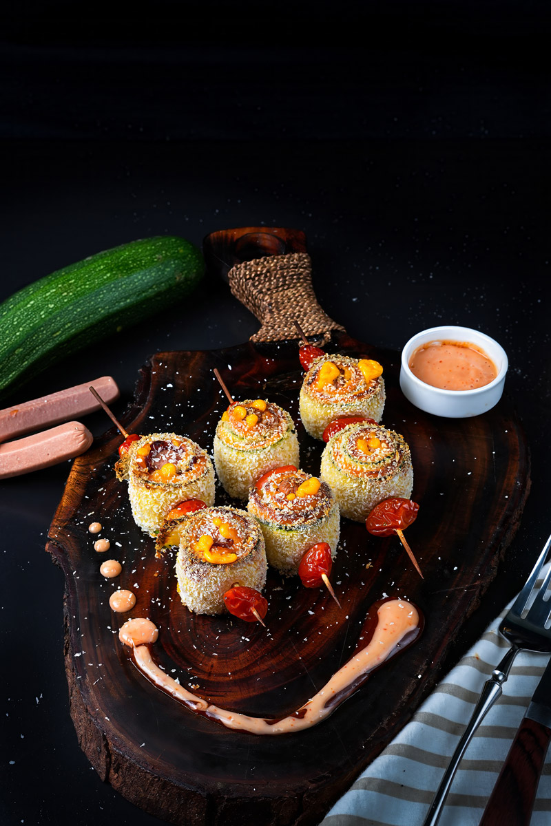 Crispy baked zucchini skewers served on a wooden board with dipping sauce and fresh ingredients.