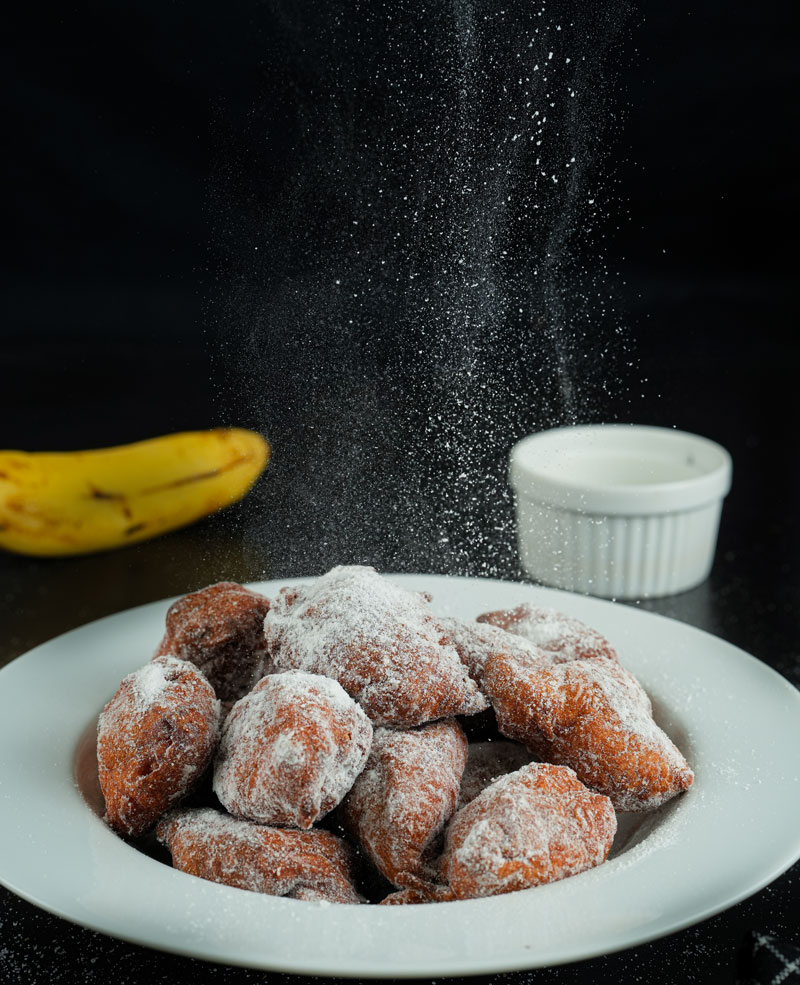 Powdered sugar being sprinkled on banana fritters