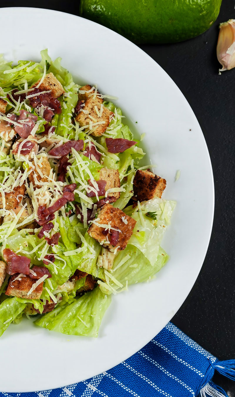 Chicken Caesar Salad with lettuce, croutons, bacon, and Parmesan on a white plate.