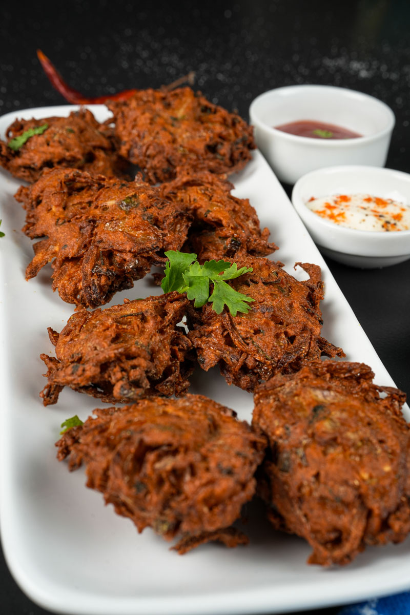 Golden brown onion fritters with cilantro garnish and dips