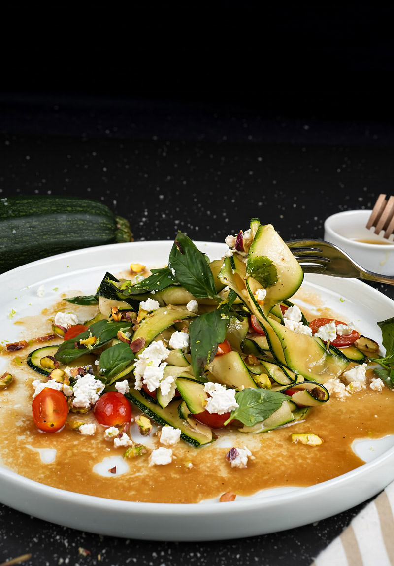 Plated raw zucchini salad with cherry tomatoes, basil, goat cheese, and pistachios.