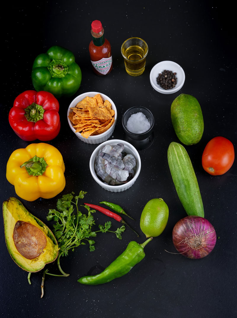 Raw ingredients for shrimp ceviche including bell peppers, avocado, limes, and Tabasco sauce