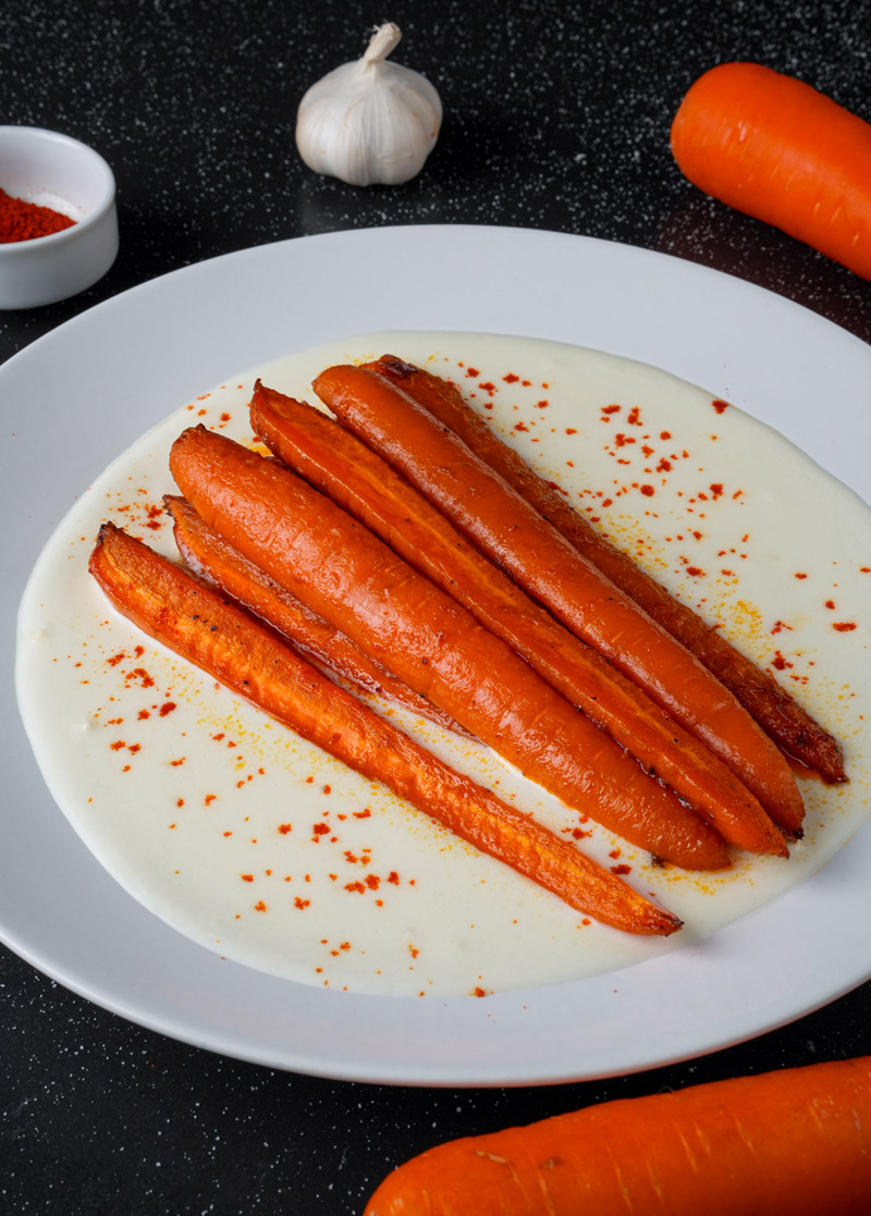 Spicy maple roasted carrots served on yogurt sauce, garnished with paprika.