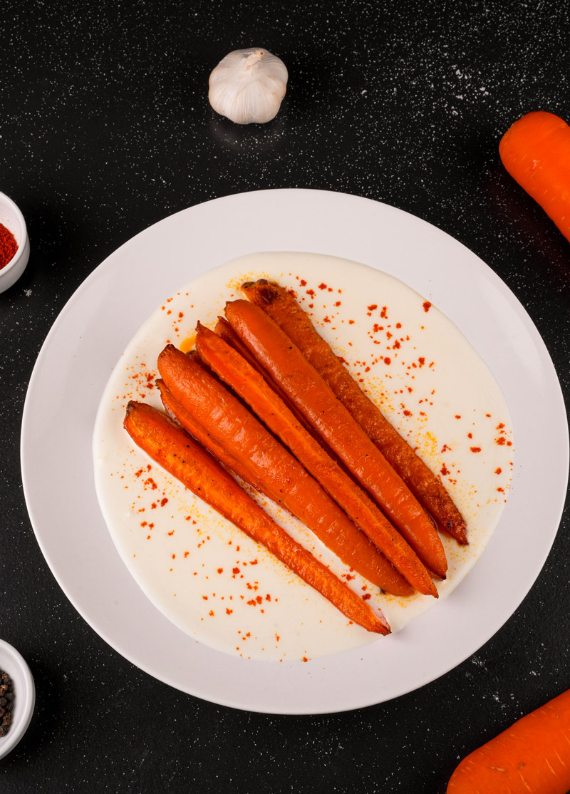 Close-up of spicy maple roasted carrots on a bed of yogurt sauce with paprika sprinkles.