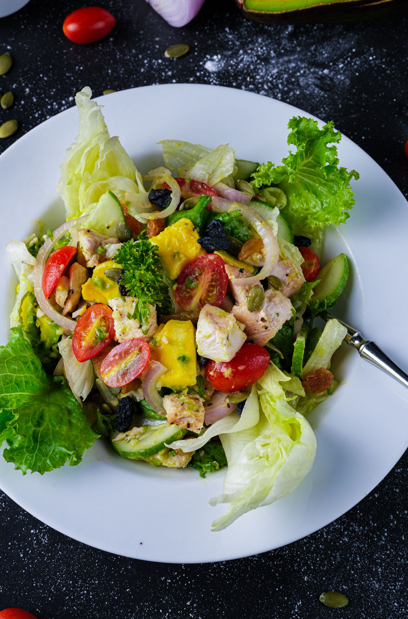 Top view of grilled chicken avocado salad with colorful ingredients on a white plate.