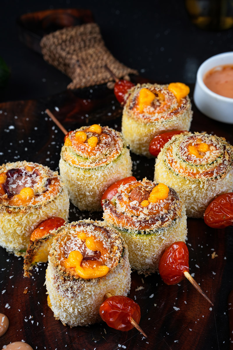 Close-up of baked zucchini skewers garnished with cheese, breadcrumbs, and cherry tomatoes.