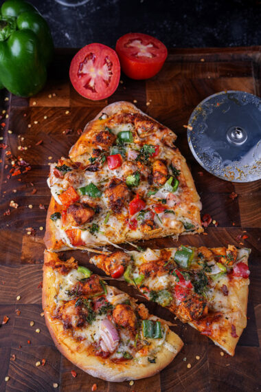 Close-up of Tandoori Paneer Pizza Naan slices on a wooden board with fresh vegetables.