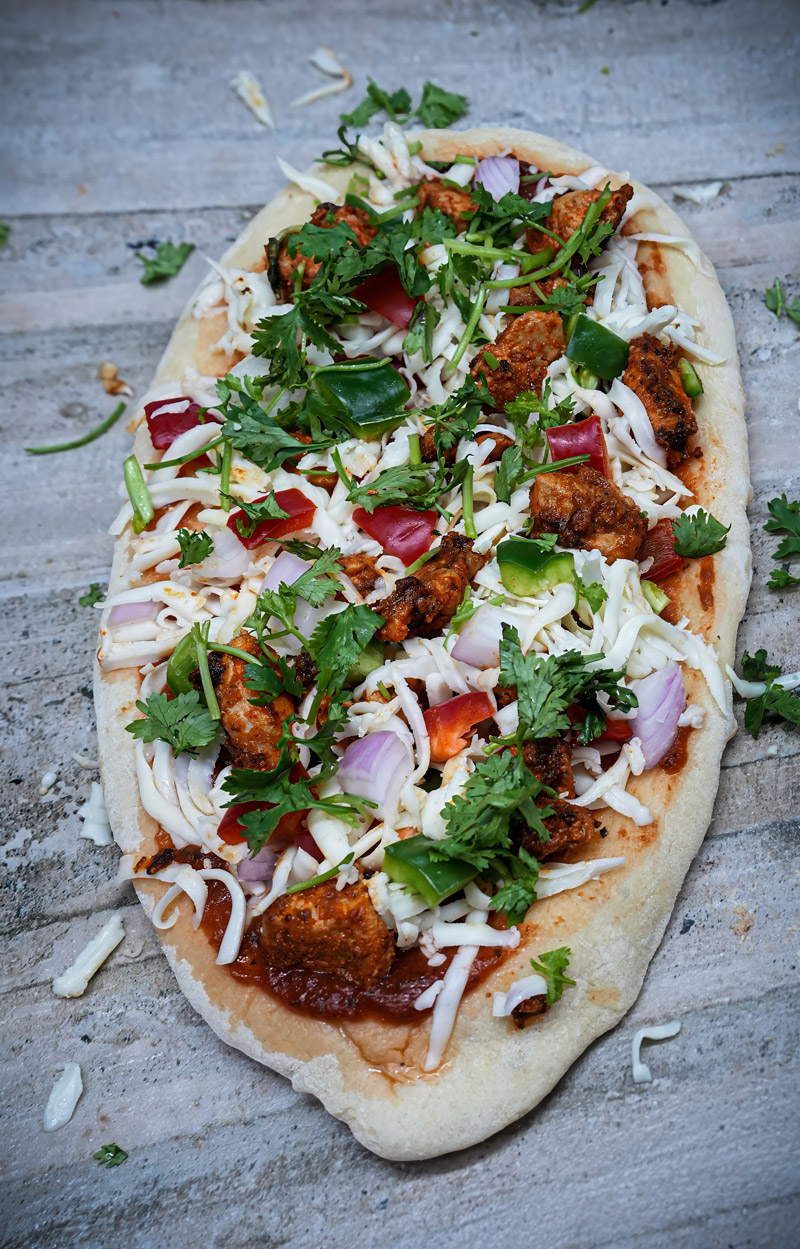 Freshly prepared Tandoori Paneer Pizza Naan topped with vegetables and cheese.