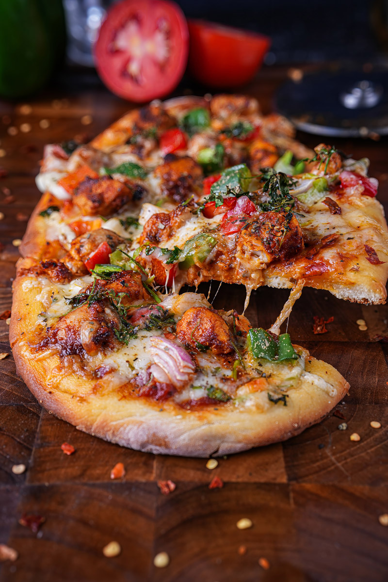 Close-up of cheesy tandoori paneer pizza naan slice being lifted with vibrant toppings