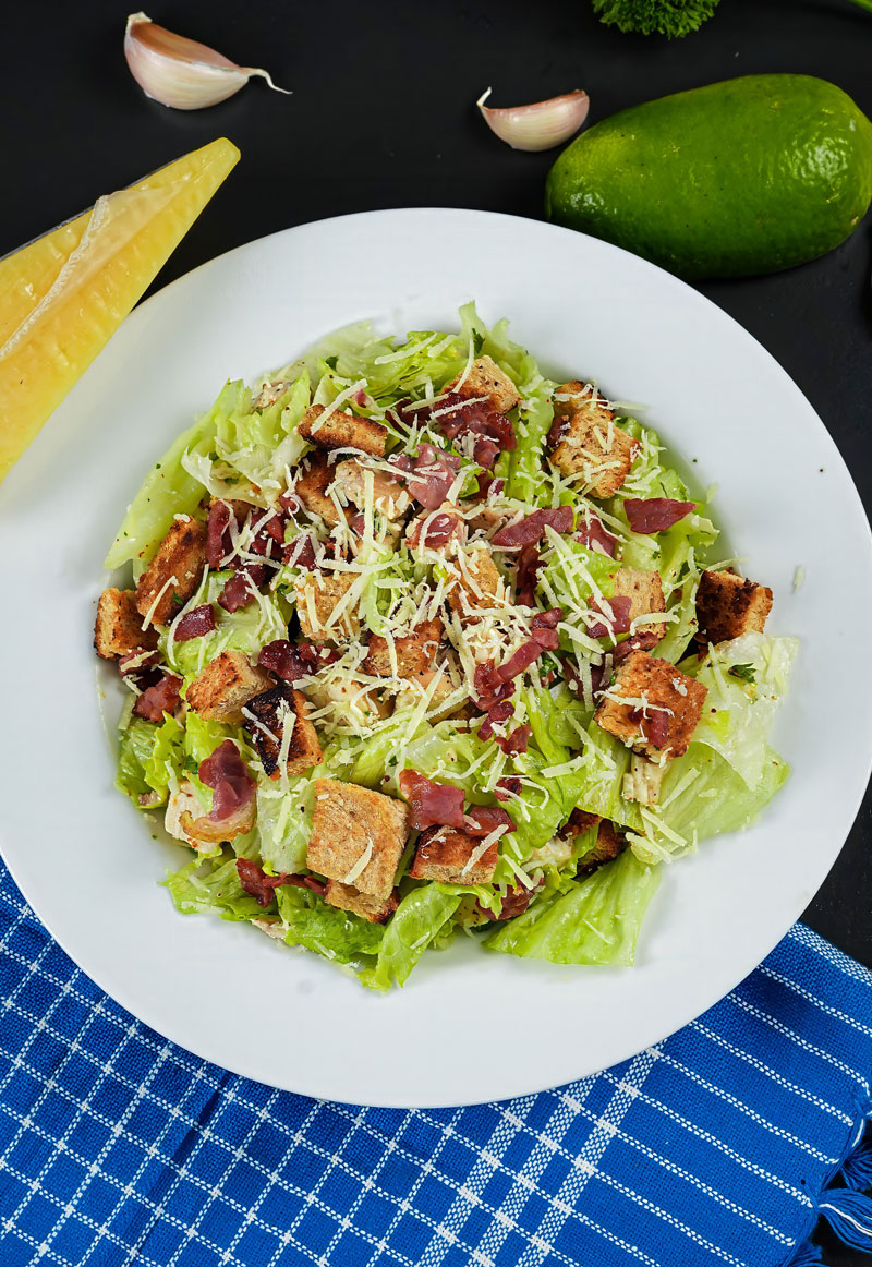 Close-up of Chicken Caesar Salad with lettuce, croutons, bacon, and grated Parmesan cheese.