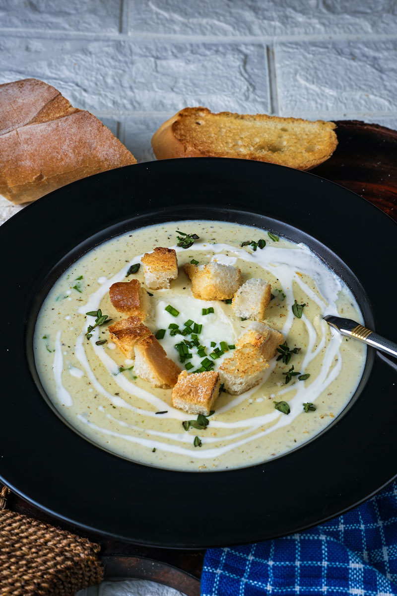 Bowl of creamy leek potato soup garnished with croutons and herbs, served with bread.