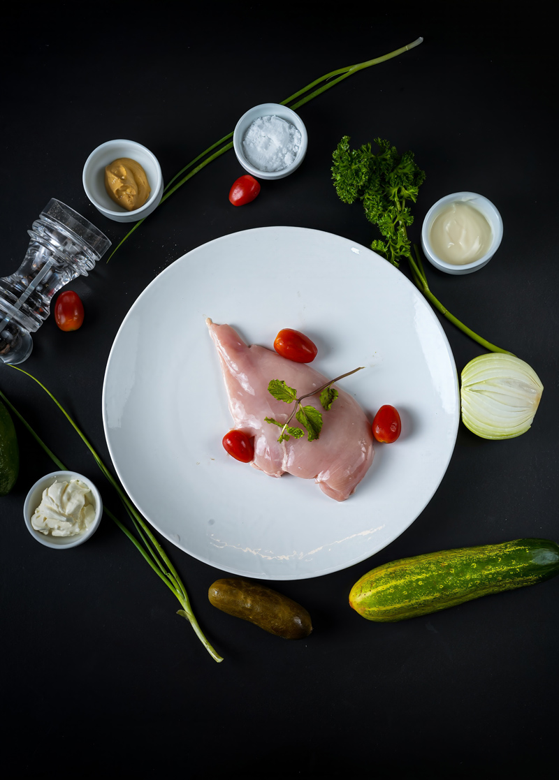 Ingredients for chicken salad, including raw chicken, herbs, and condiments.