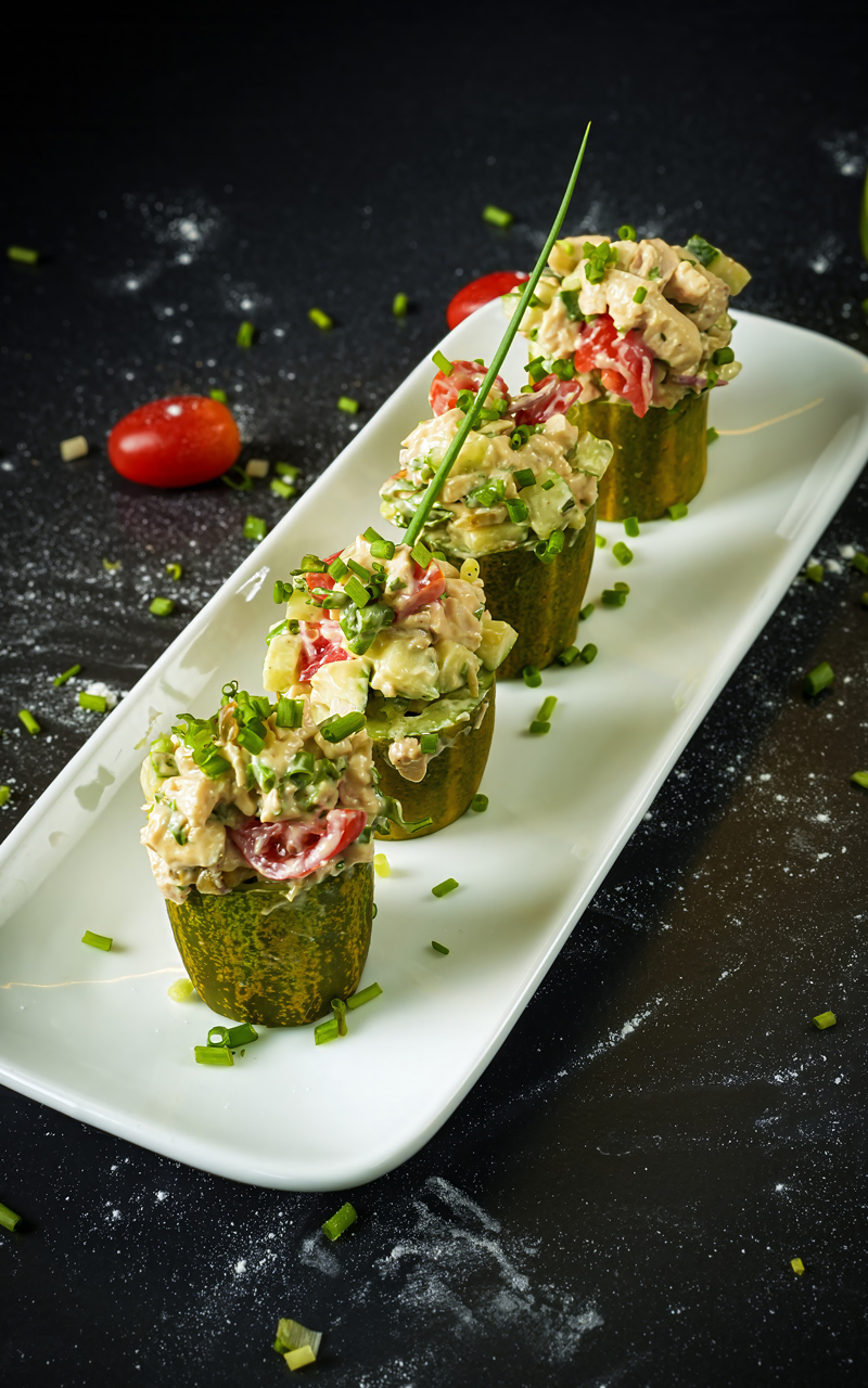 Plated chicken salad cucumber cups with a garnish of chopped greens.