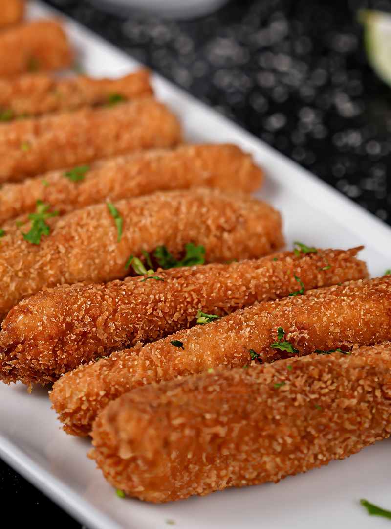 Close-up of crispy fish sticks garnished with parsley on a white plate.