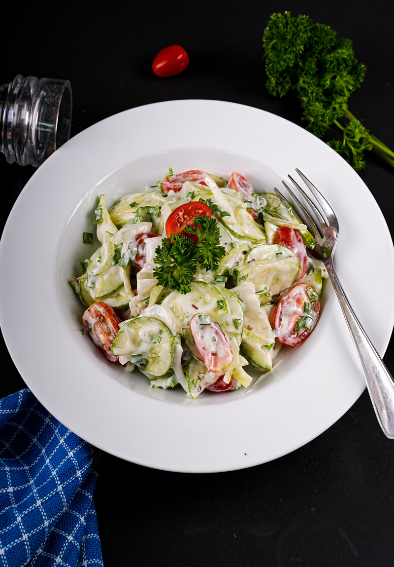 Vibrant salad with cucumber, tomatoes, and creamy dressing in a serving dish.