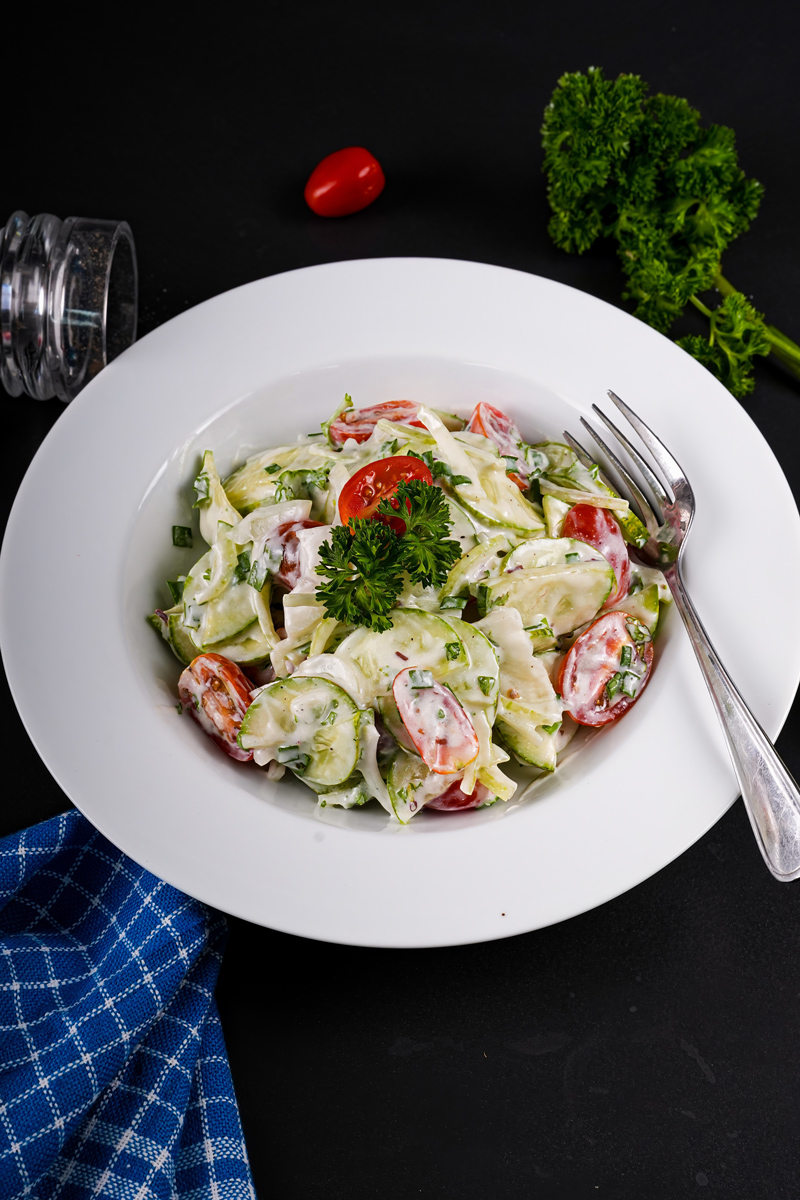 Healthy cucumber tomato salad with creamy dressing and fresh garnishes.