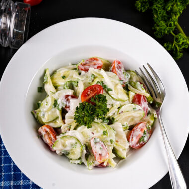 Bowl of creamy cucumber tomato salad garnished with fresh parsley.