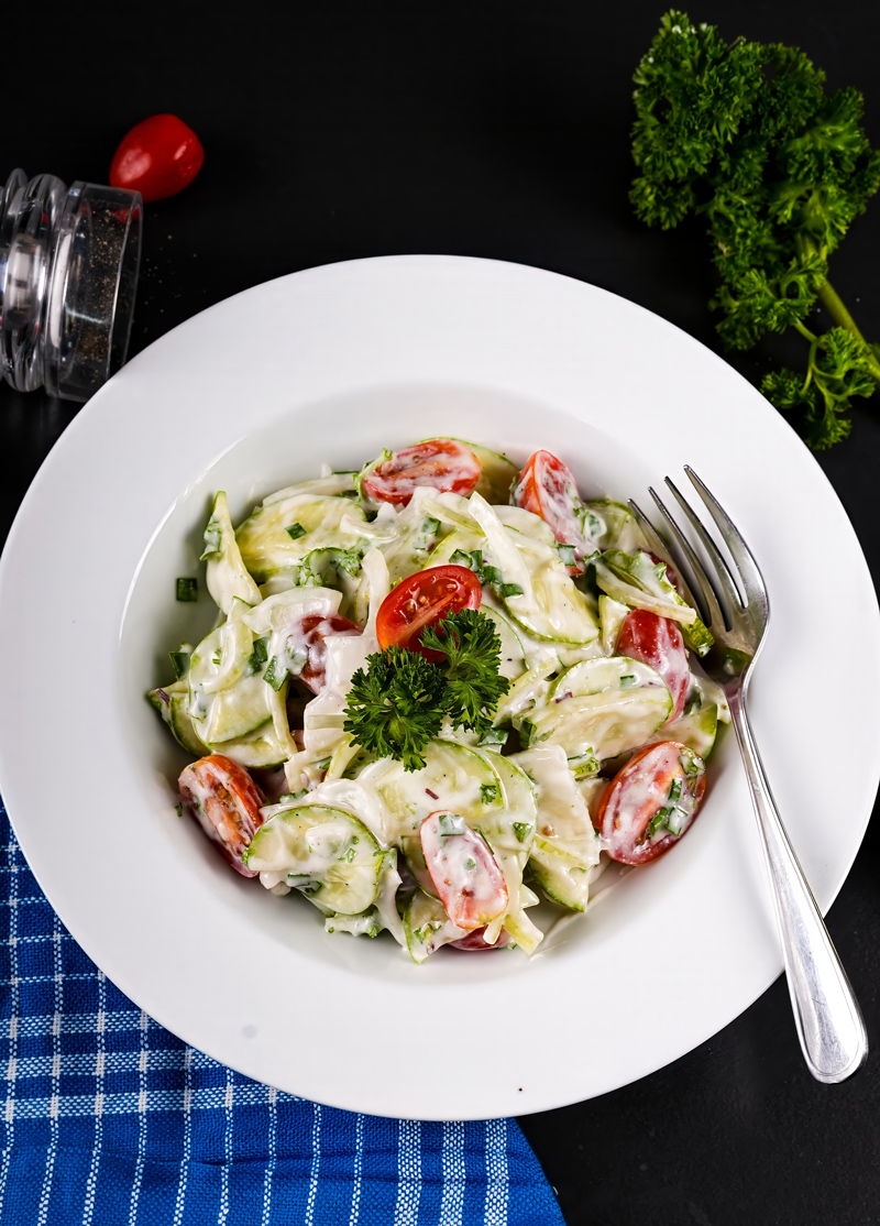 Bowl of creamy cucumber tomato salad garnished with fresh parsley.