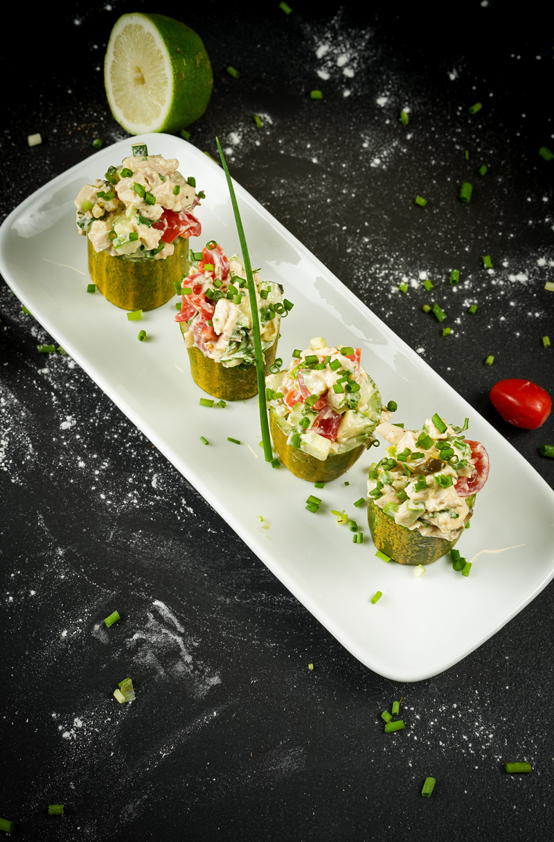 Close-up view of chicken salad cucumber cups on a white serving plate.